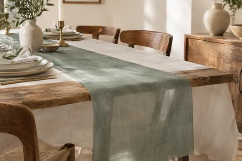 Chemin de table vert eucalyptus légèrement translucide posé sur une nappe claire et une table en bois