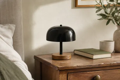 Lampe à poser noire en métal laqué avec base circulaire en bois, installée sur une table de chevet