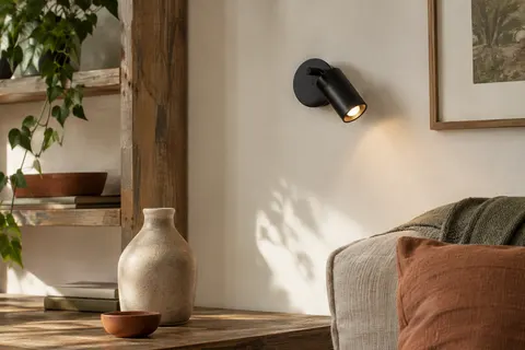Applique murale compacte en métal noir mat, orientable, installée sur un mur ivoire près d’une étagère.