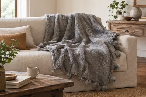 Plaid Bedsure gris en polyester posé sur un canapé clair, avec sa texture douce et ses pompons décoratifs.