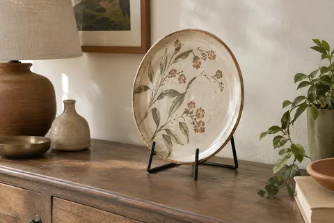 Chevalet noir mat en métal présentant une assiette décorative sur une console en bois patiné.