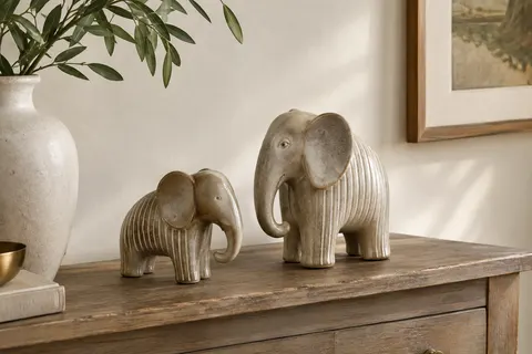 Duo d’éléphants décoratifs en céramique beige et grise posé sur une console en bois patiné.