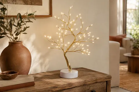 Lampe arbre aux branches dorées et LED blanc chaud posée sur une console en bois.