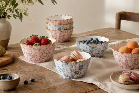 Bols en papier à motifs floraux pastel rose et bleu, avec un bord festonné doré, disposés sur une table en bois