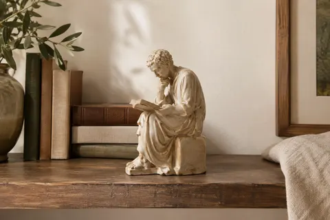 Sculpture beige en résine représentant un penseur qui lit, posée sur une étagère en bois.