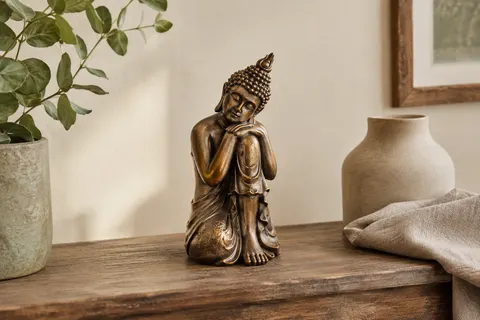 Statuette de Bouddha penseur en résine bronze posée sur une console en bois patiné