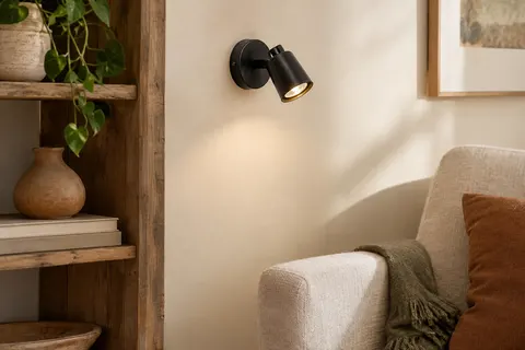Applique murale noire orientable en métal installée sur un mur ivoire près d’un fauteuil en lin