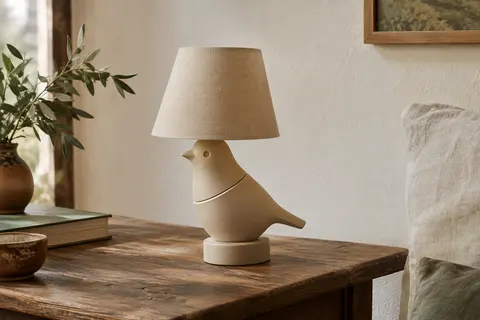 Lampe de table beige en forme d’oiseau, posée sur une table en bois près d’un mur ivoire.