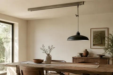 Système de suspension noir mat au plafond, avec une lampe suspendue au-dessus d’une table en bois patiné.